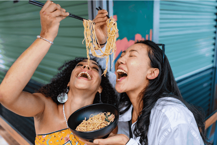 Friends smile while sharing a bowl of ramen